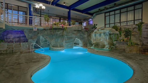 Una piscina interior con una fuente azul, una cascada y una escalera que lleva a un balcón.