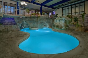 An indoor swimming pool with a blue water feature, a waterfall, and a staircase leading to a balcony.