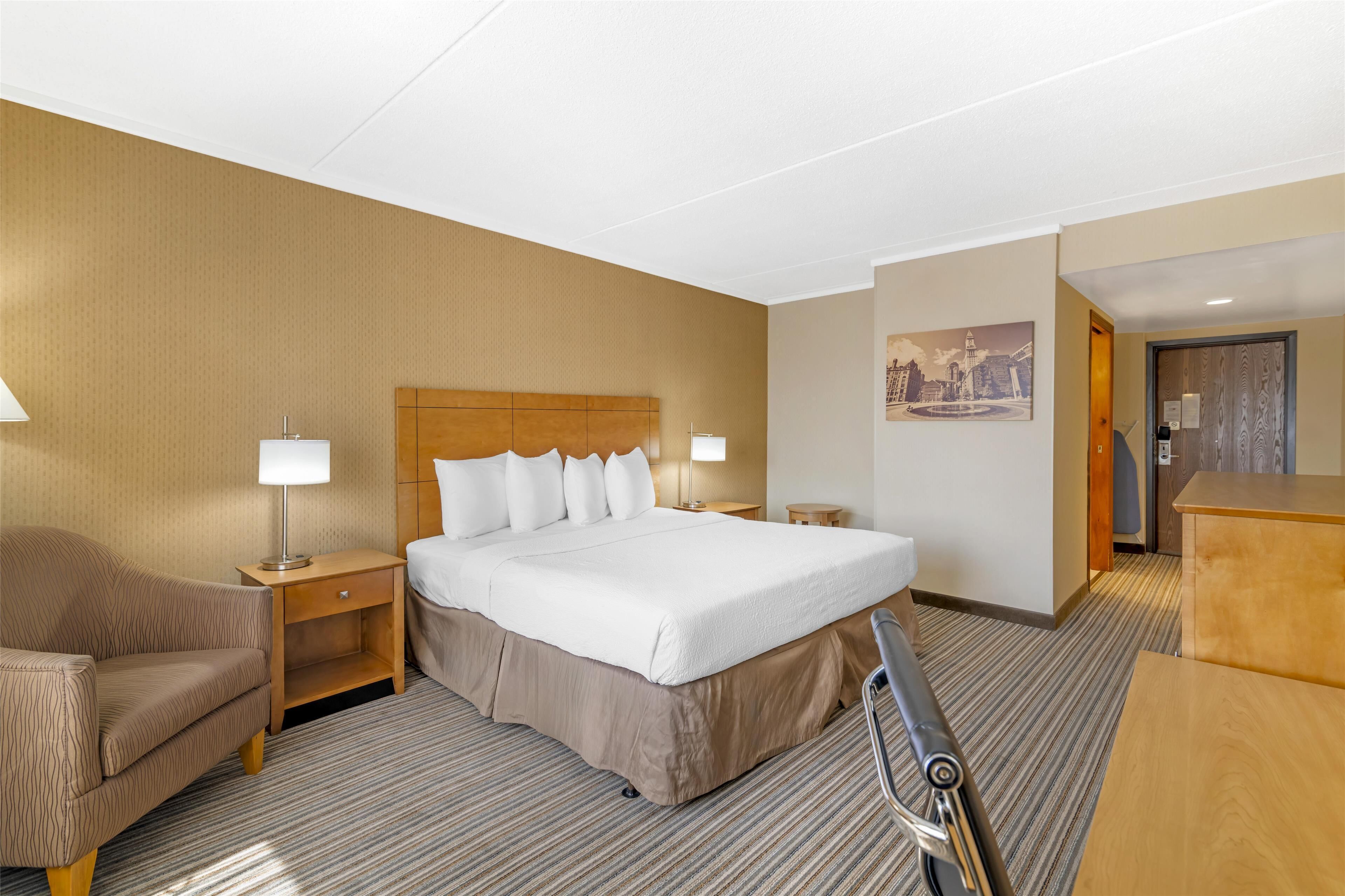 Une chambre d’hôtel avec un grand lit, deux tables de chevet, une chaise, un bureau et un tableau au mur.
