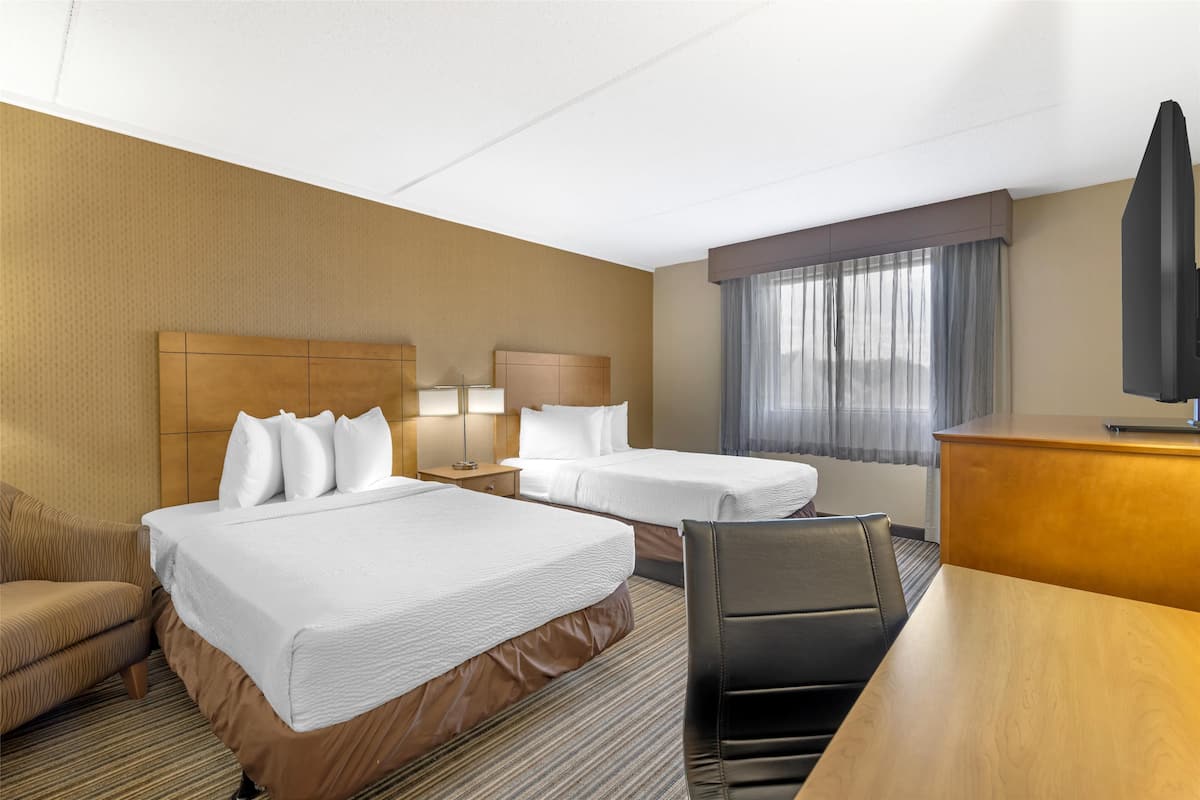 Een hotelkamer met twee bedden, een bureau, een stoel, een televisie en een raam met gordijnen.
