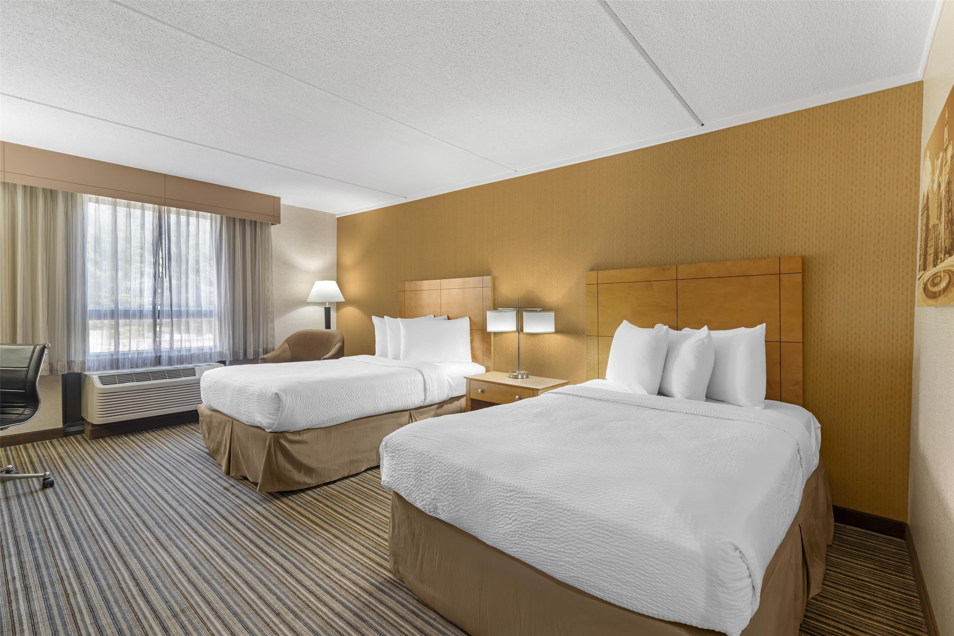 Habitación de hotel con dos camas, un escritorio, una silla y un ventanal con cortinas.