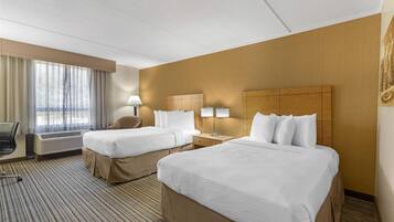 Habitación de hotel con dos camas, un escritorio, una silla y un ventanal con cortinas.