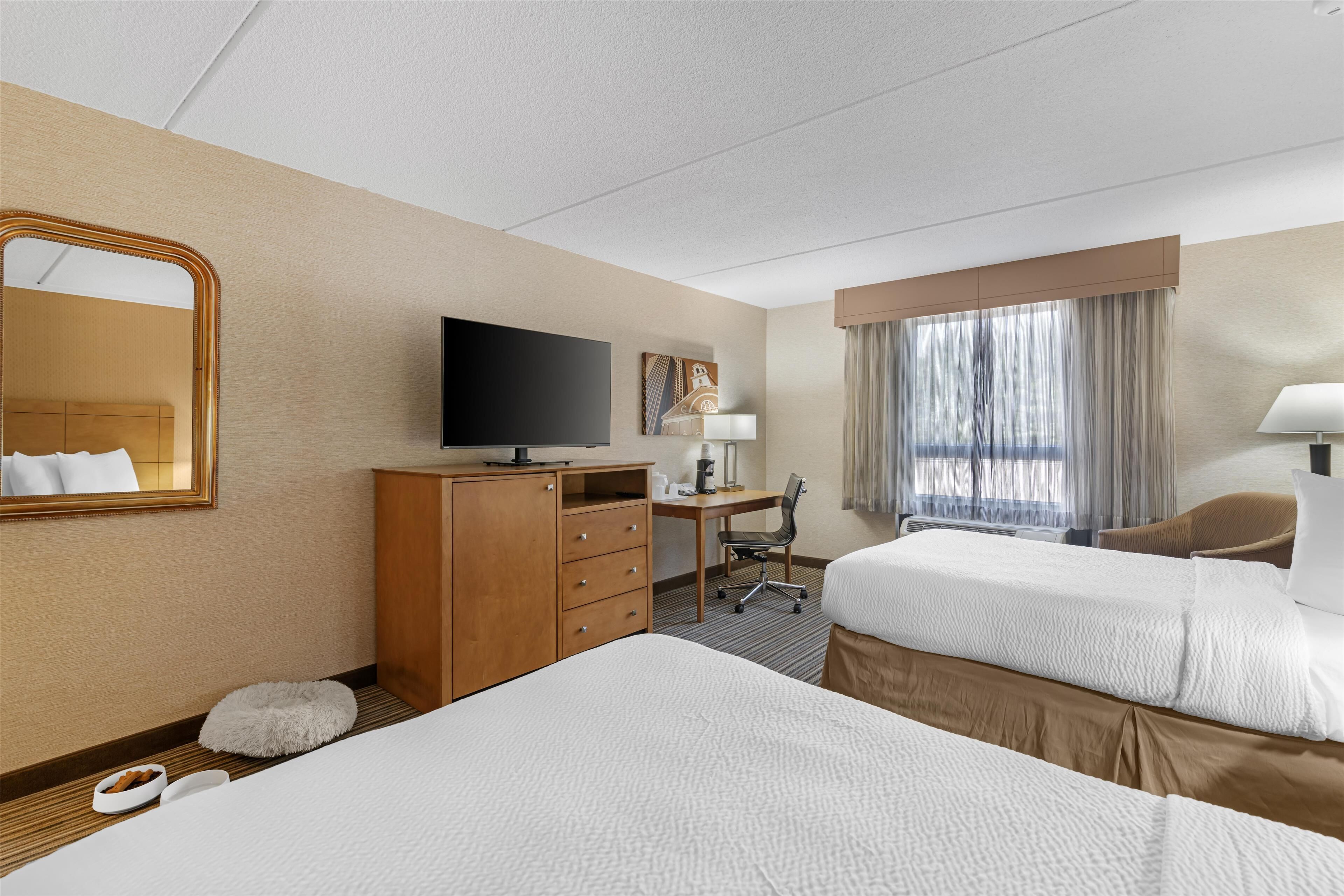 A hotel room with two beds, a desk, a TV, a mirror, and a window with curtains.