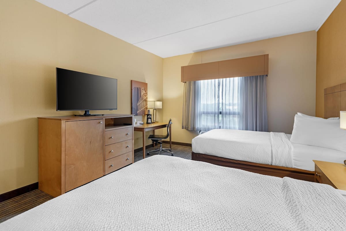Een hotelkamer met twee bedden, een televisie, een bureau met stoel en een raam met gordijnen.