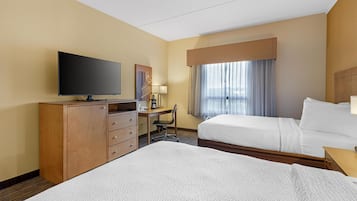 A hotel room with two beds, a TV, a desk with a chair, and a window with curtains.