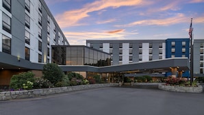 A modern hotel with a glass facade, a covered entrance, and a flagpole with an American flag.