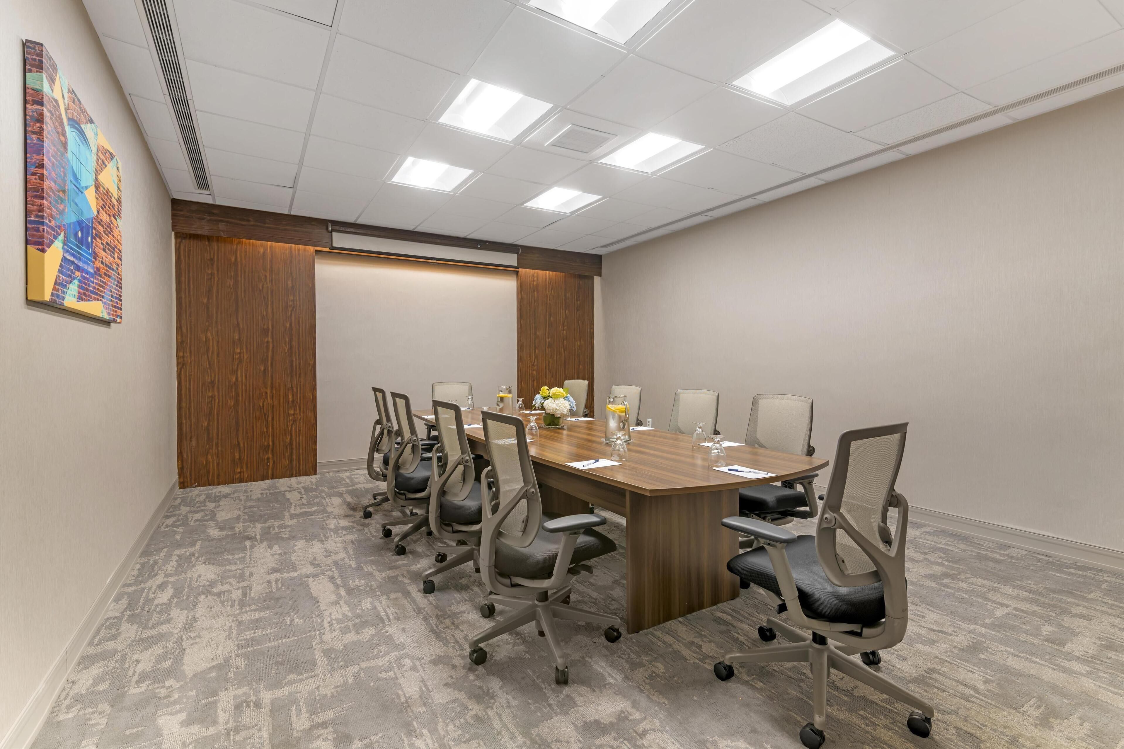 A conference room with a long table, six chairs, and a wooden accent wall.