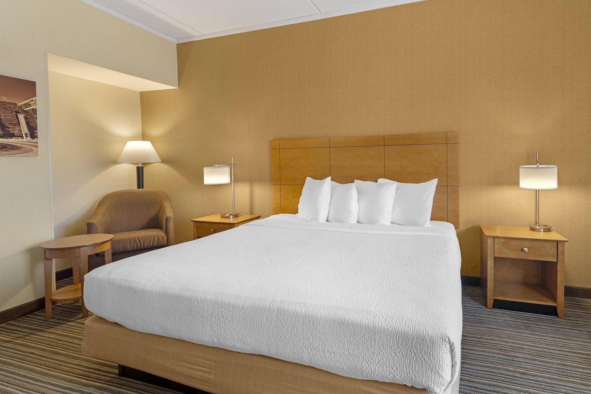 Een hotelkamer met een groot bed, twee nachtkastjes met lampen, een stoel en een kleine tafel.