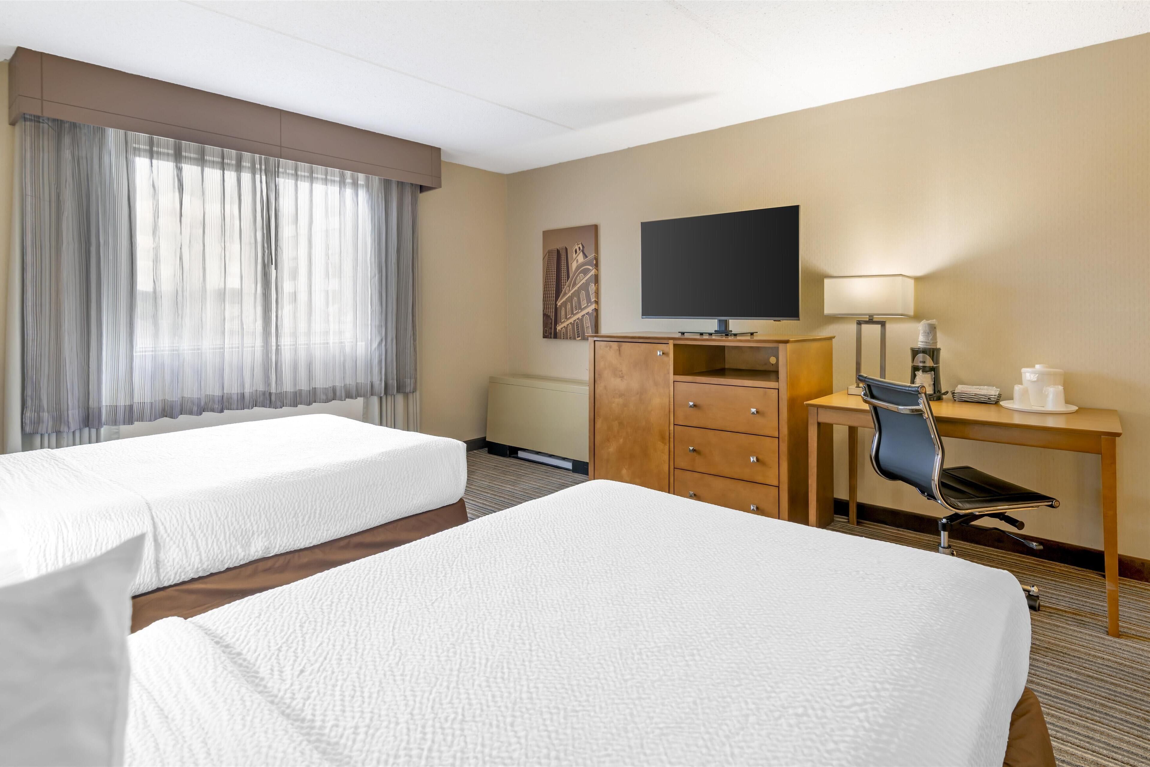 Una habitación de hotel con dos camas, un escritorio con silla, un televisor y una lámpara.