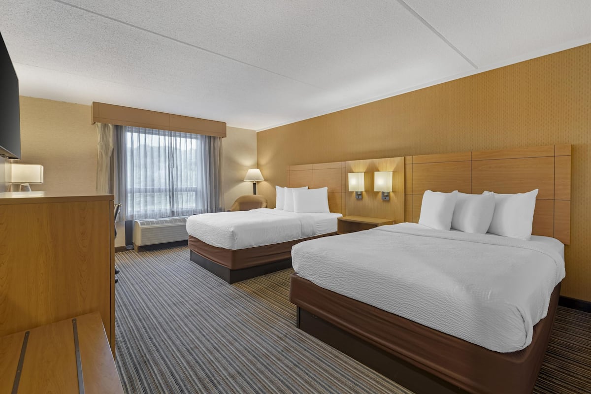 Een hotelkamer met twee bedden, een bureau, een televisie en een raam met gordijnen.
