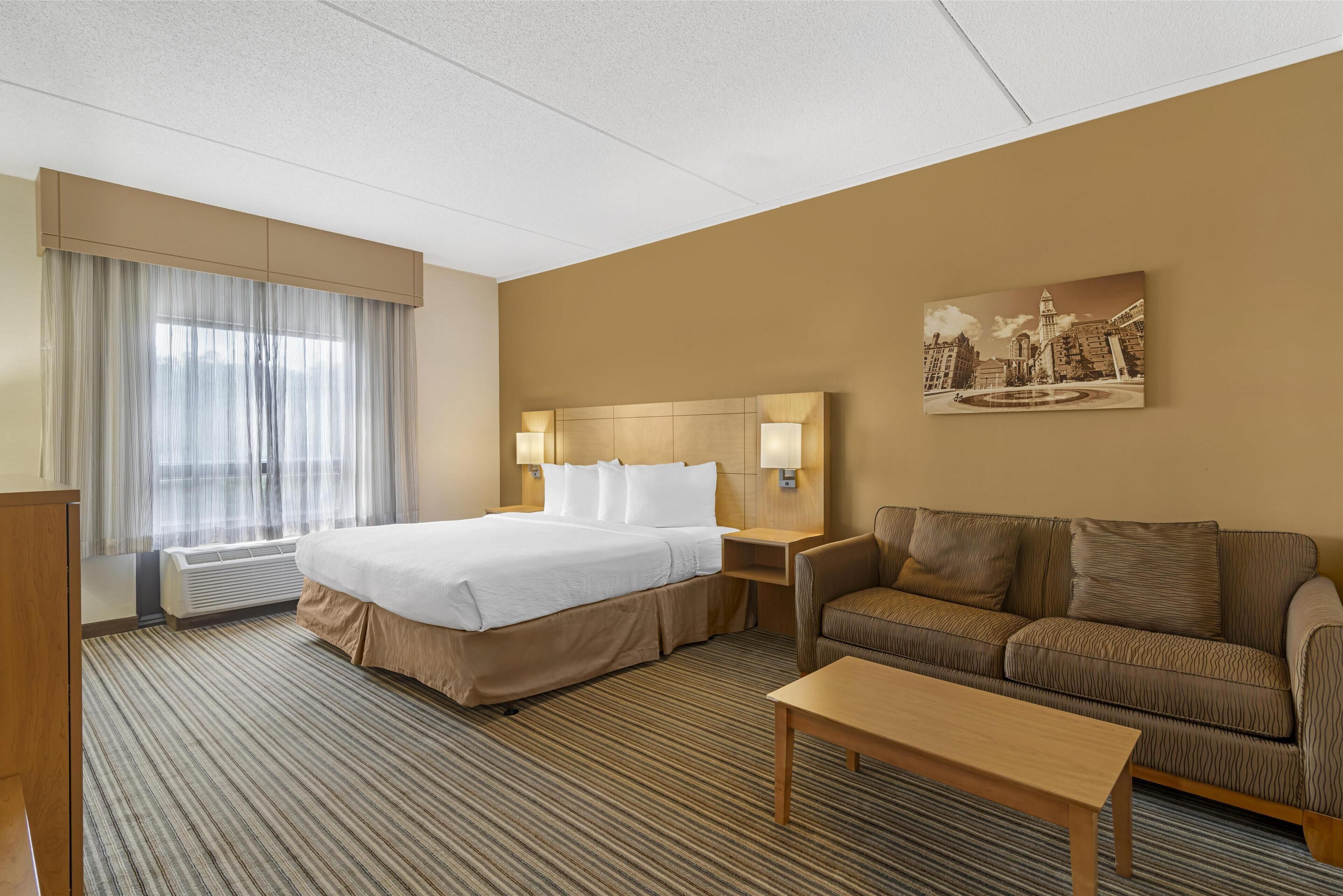 A hotel room with a large bed, a sofa, a coffee table, and a painting on the wall.