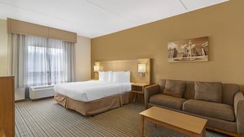 A hotel room with a large bed, a sofa, a coffee table, and a painting on the wall.