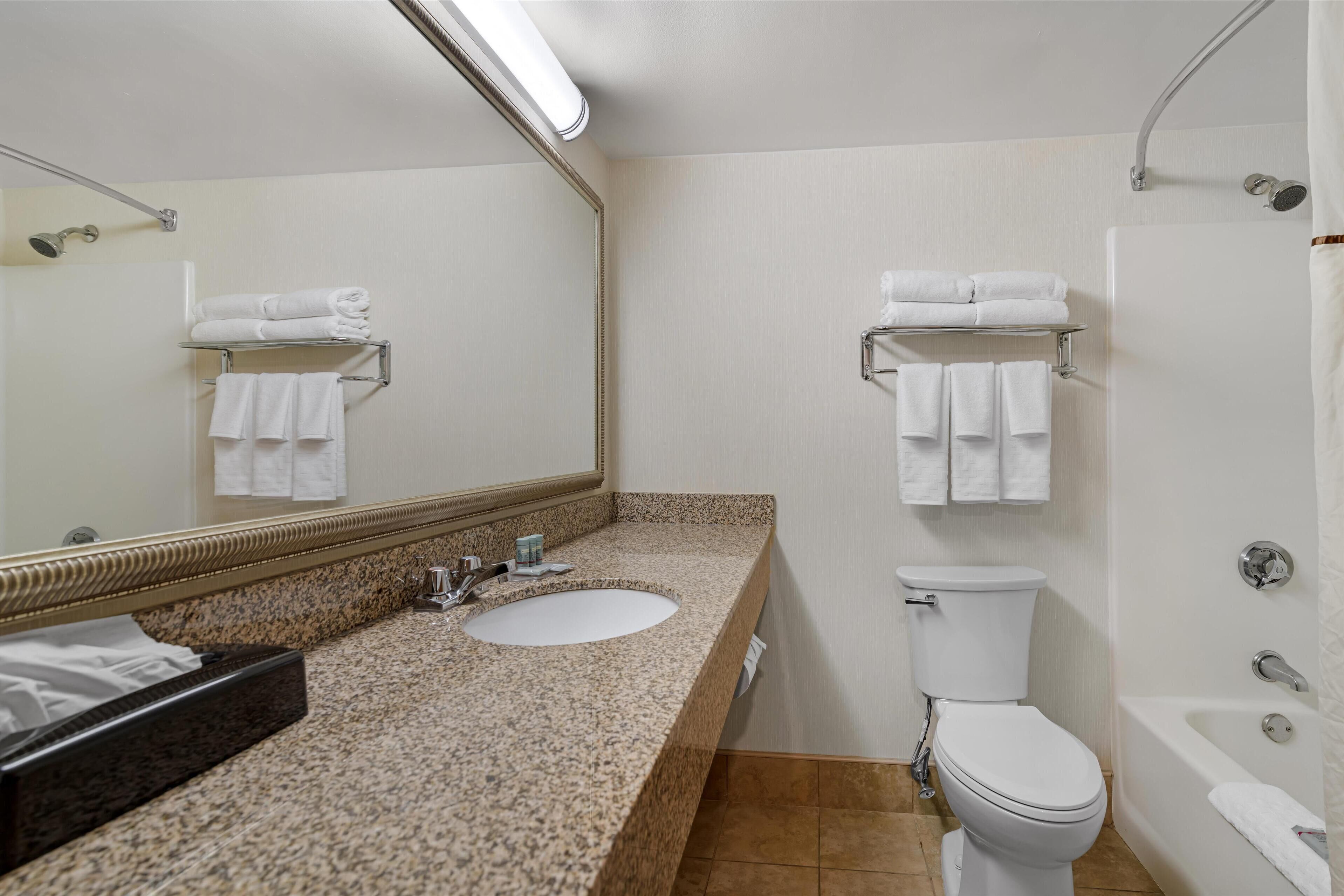 A bathroom with a granite countertop sink, a toilet, a bathtub, and a mirror with a towel rack above the sink.
