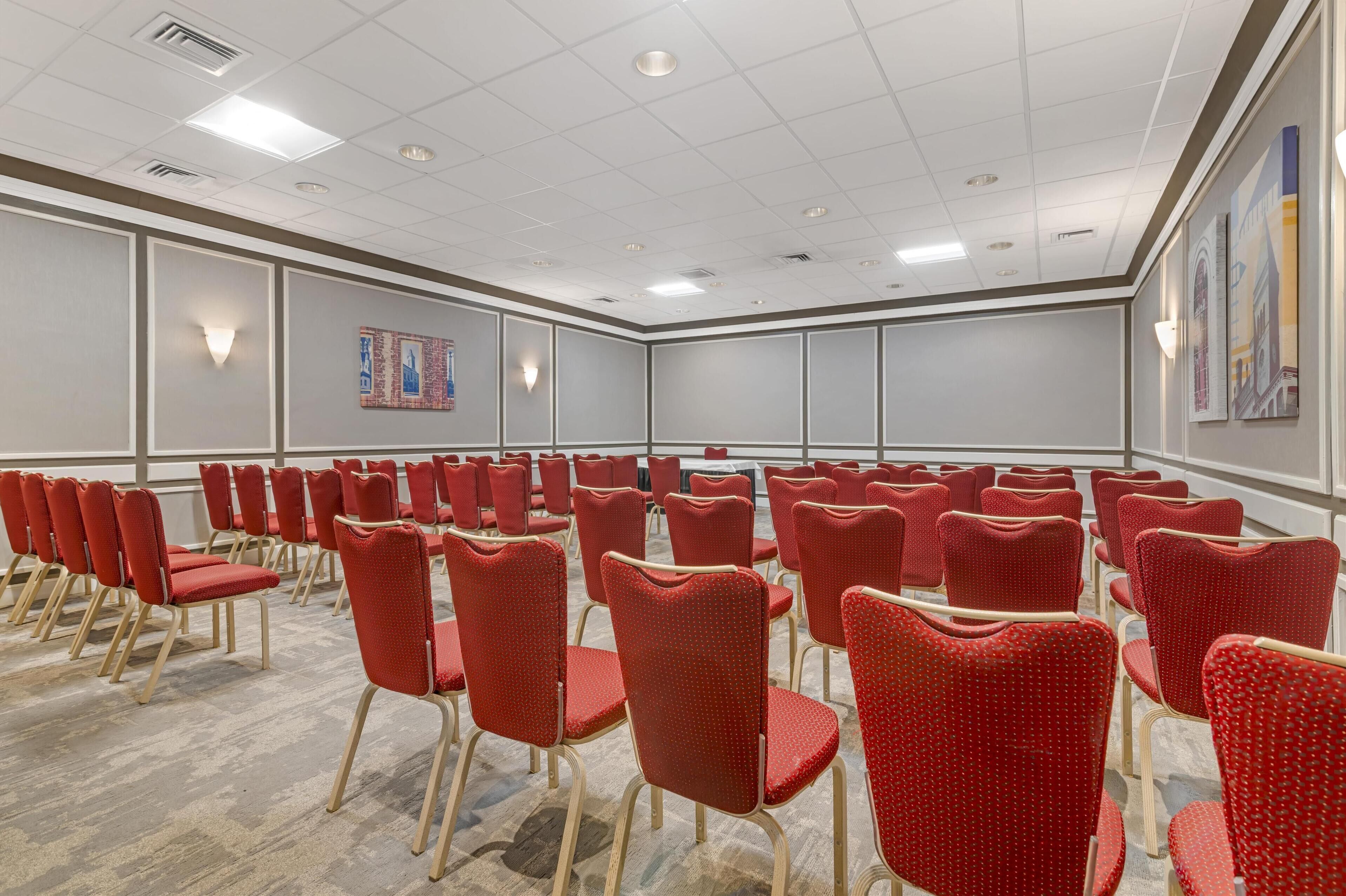 A conference room with rows of red chairs and a carpeted floor.