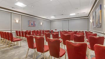 A conference room with rows of red chairs and a carpeted floor.