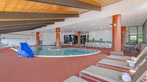 An indoor swimming pool area with lounge chairs, a covered seating area, and a view of the pool.