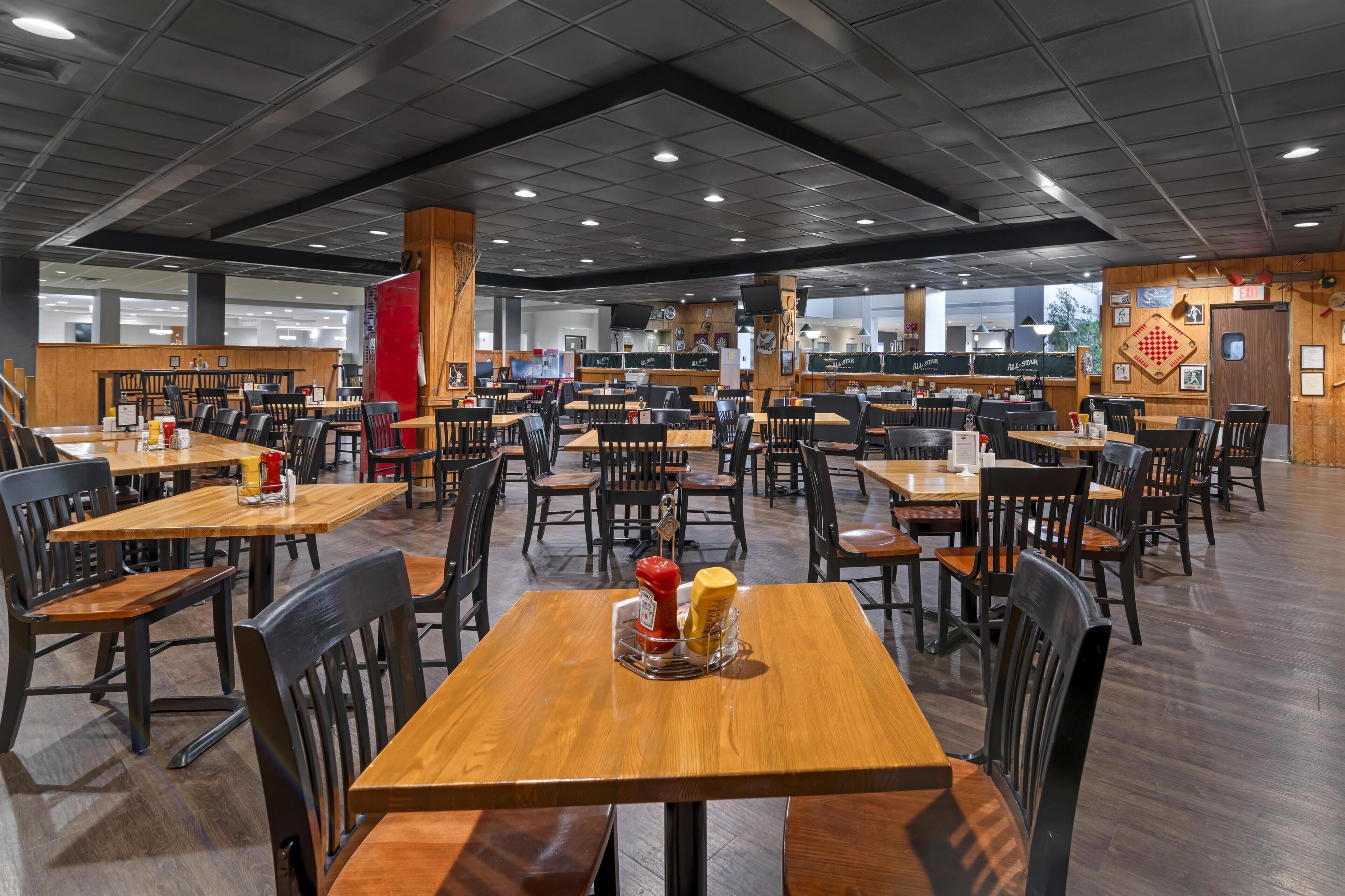 Una amplia cafetería con numerosas mesas y sillas, suelo de madera y un techo alto con iluminación empotrada.