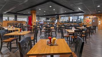 Una amplia cafetería con numerosas mesas y sillas, suelo de madera y un techo alto con iluminación empotrada.