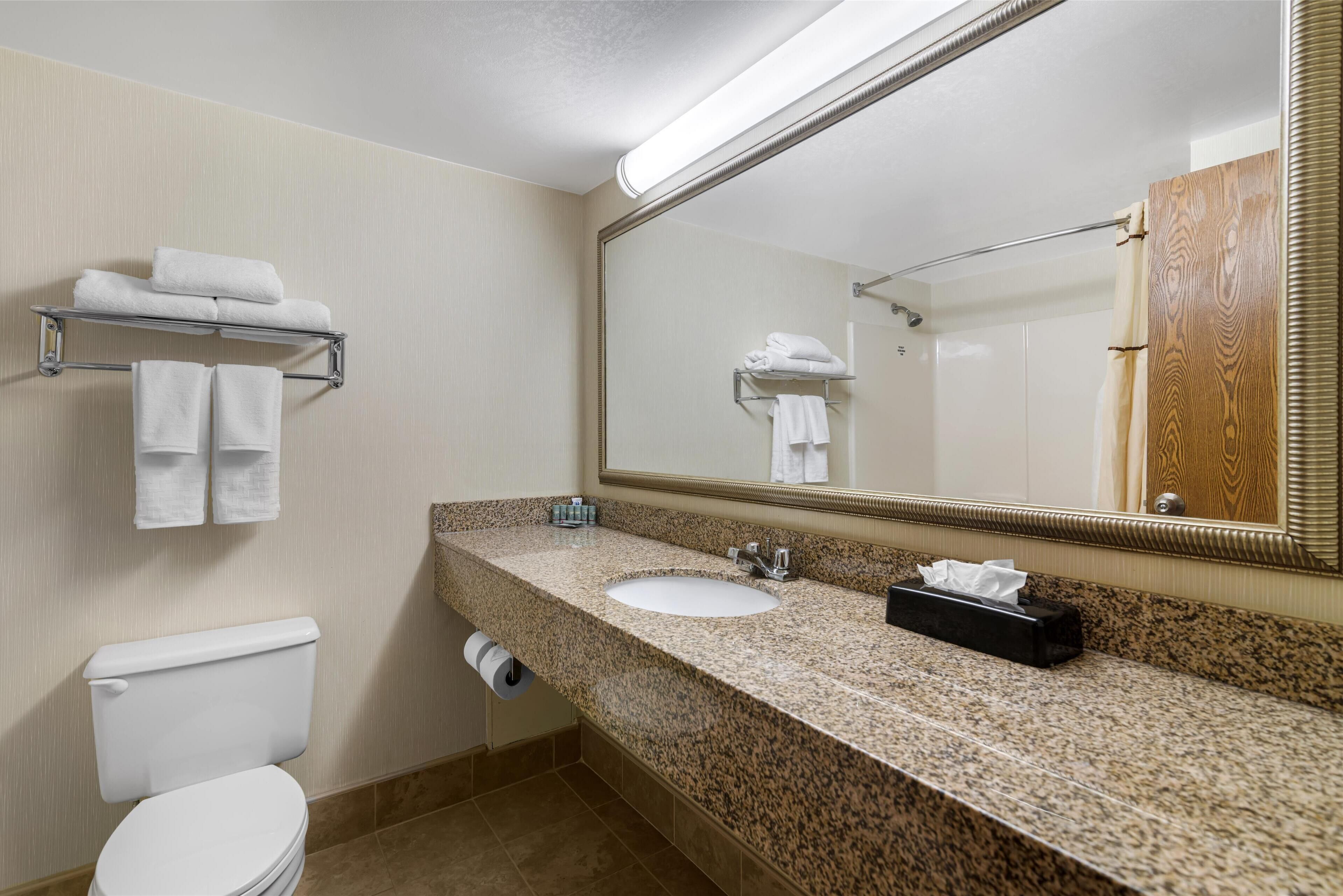 Une salle de bain avec des toilettes blanches, un lavabo avec un miroir au-dessus et des serviettes sur une étagère.
