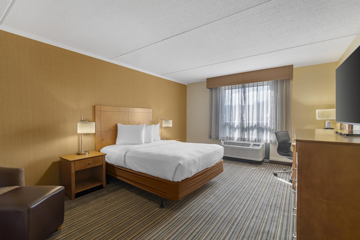 Een hotelkamer met een bed, een bureau, een stoel, een nachtkastje en een raam met gordijnen.
