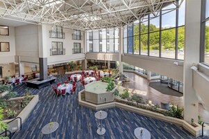 Un espacio interior amplio con varias mesas y sillas para comer, una zona central de asientos y grandes ventanales con vistas al exterior.
