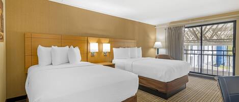 A hotel room with two beds, a wooden headboard, a nightstand, a lamp, and a view of the outside through large windows.