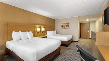 A hotel room with two beds, a desk, a chair, and a TV.