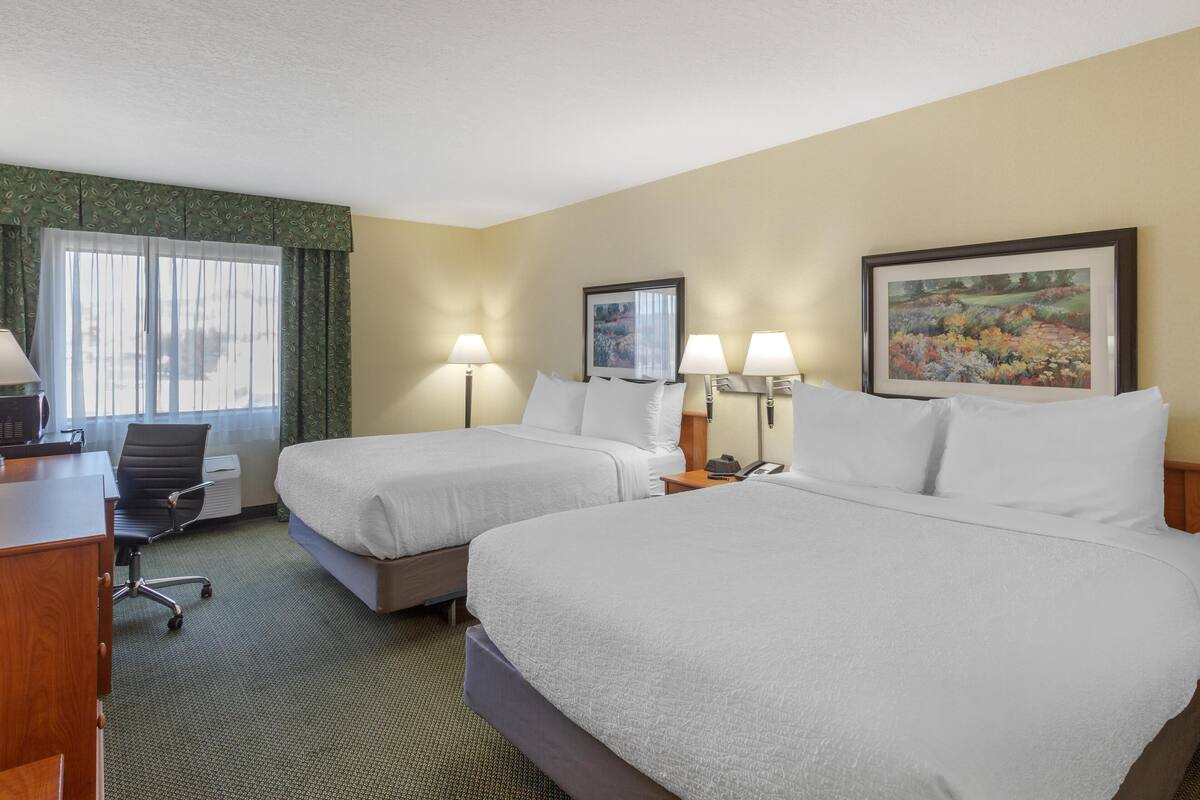 A hotel room with two beds, a desk with a computer, a chair, and a window with curtains.