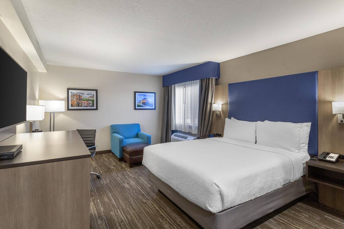 A hotel room with a bed, a desk, a chair, and two wall-mounted lamps.