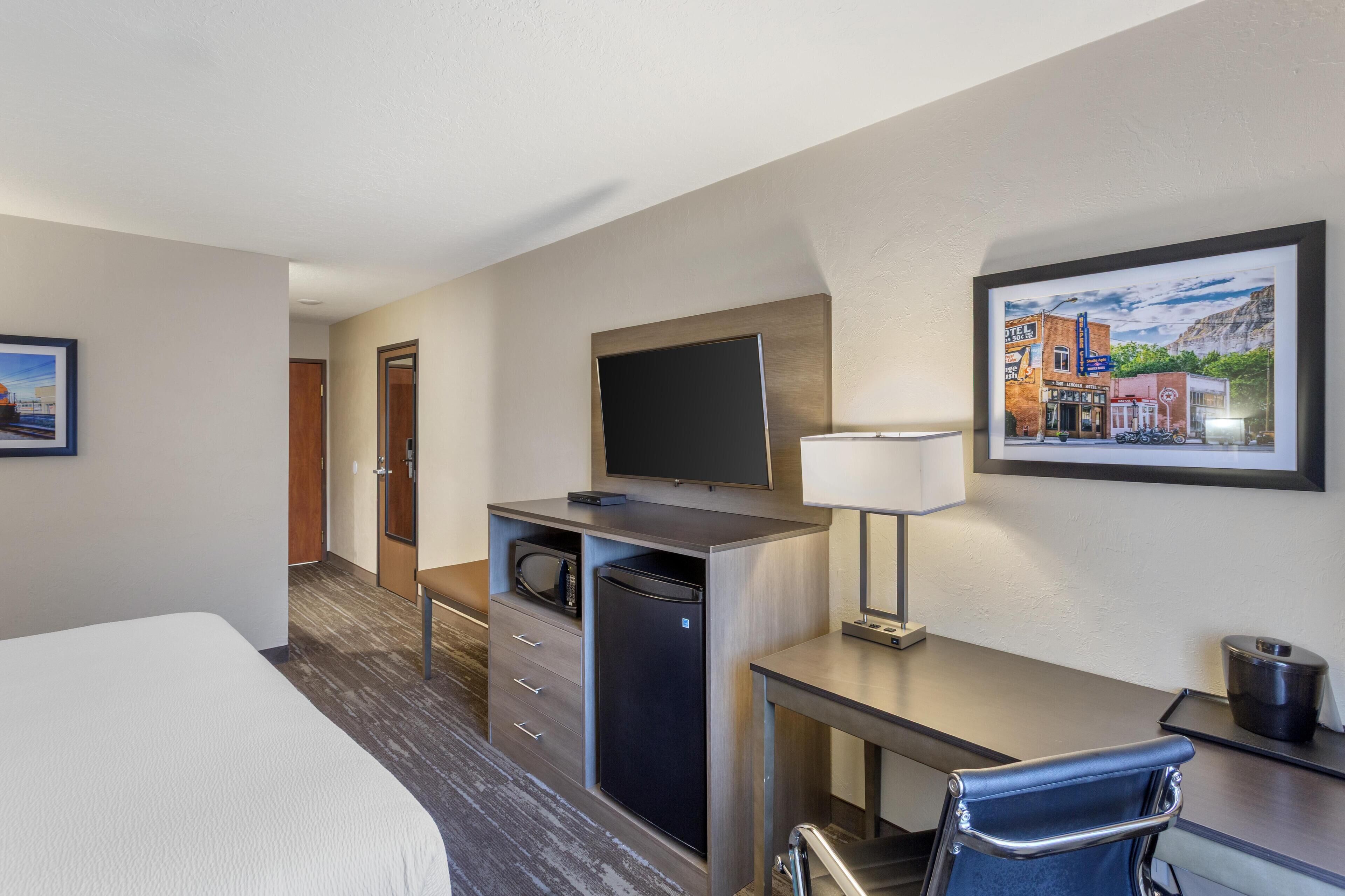 A hotel room with a bed, a desk with a computer, a microwave, and a TV.