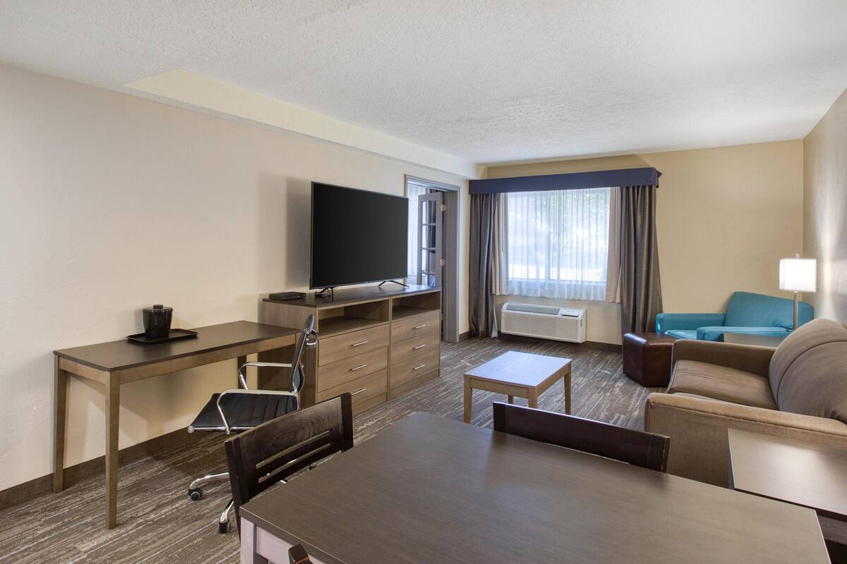 A hotel room with a dining table, a TV, a sofa, a small table, and a window with curtains.
