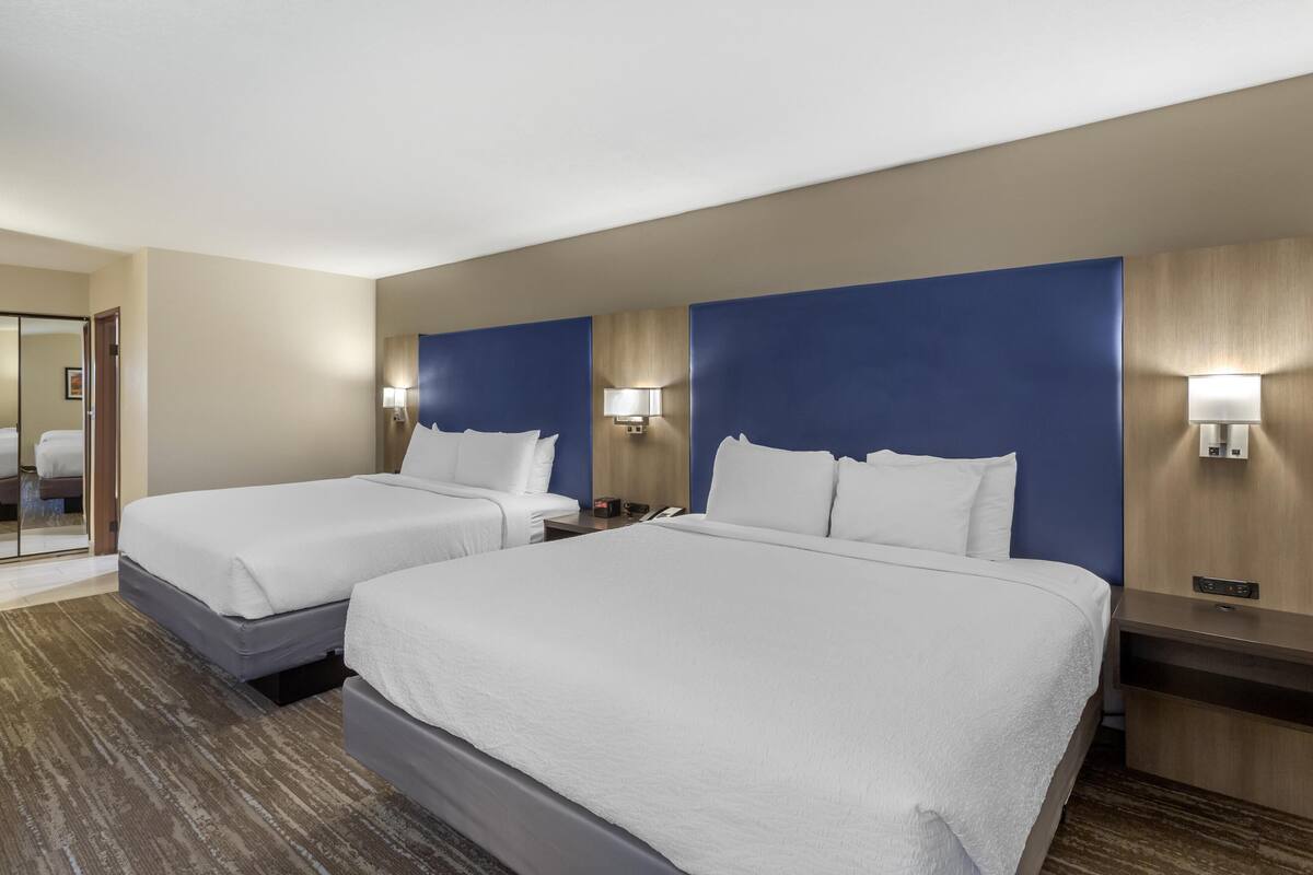 A hotel room with two beds, a wooden headboard, bedside lamps, a nightstand, and a mirror.