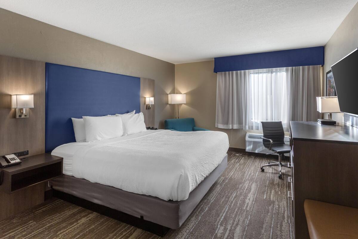 A hotel room with a large bed, a desk, a chair, and a TV.