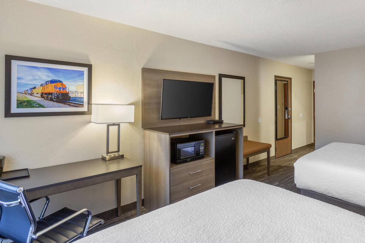 A hotel room with a bed, a desk with a chair, a television, a microwave, and a door.