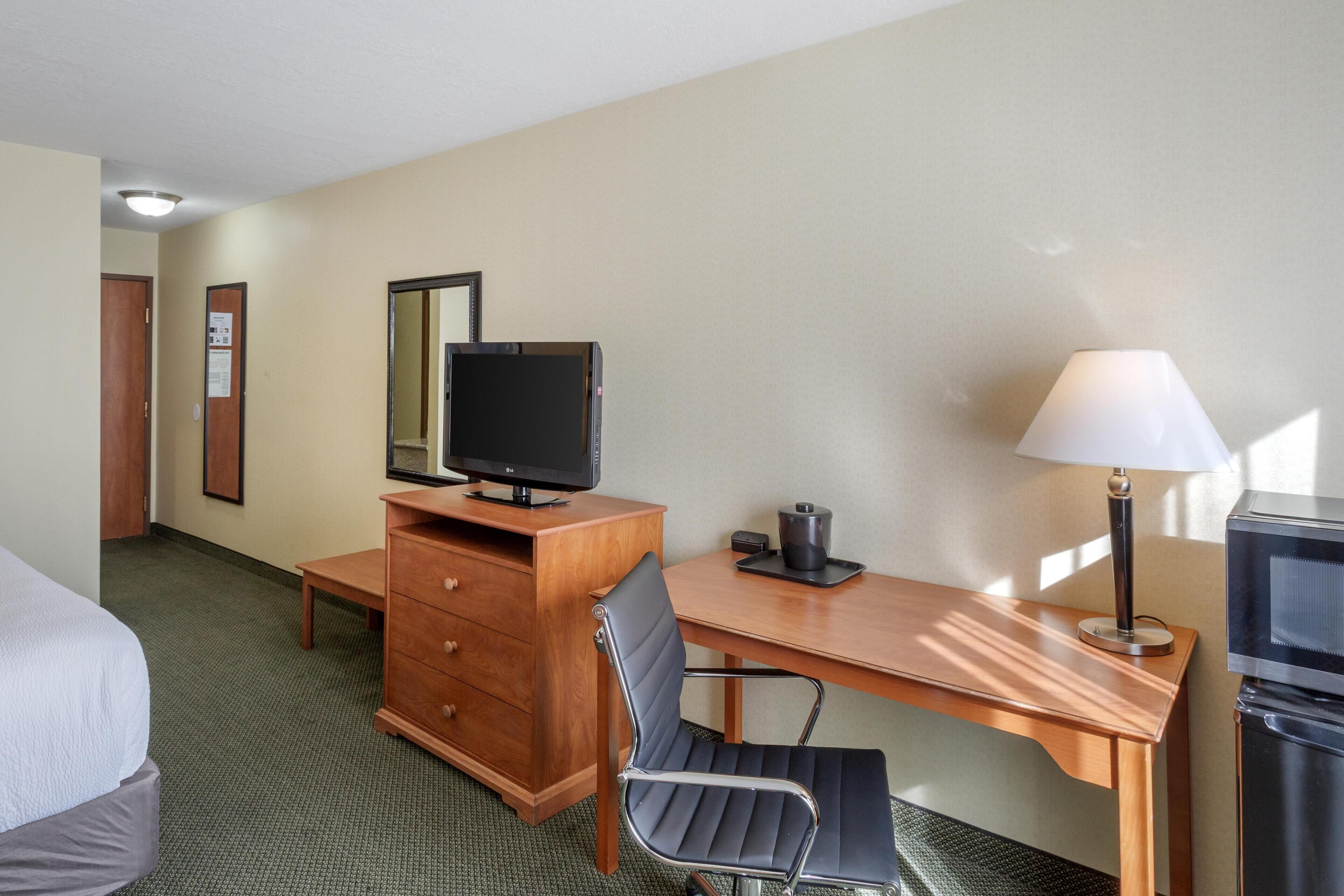 A hotel room with a bed, a desk with a computer, a chair, a lamp, and a TV.