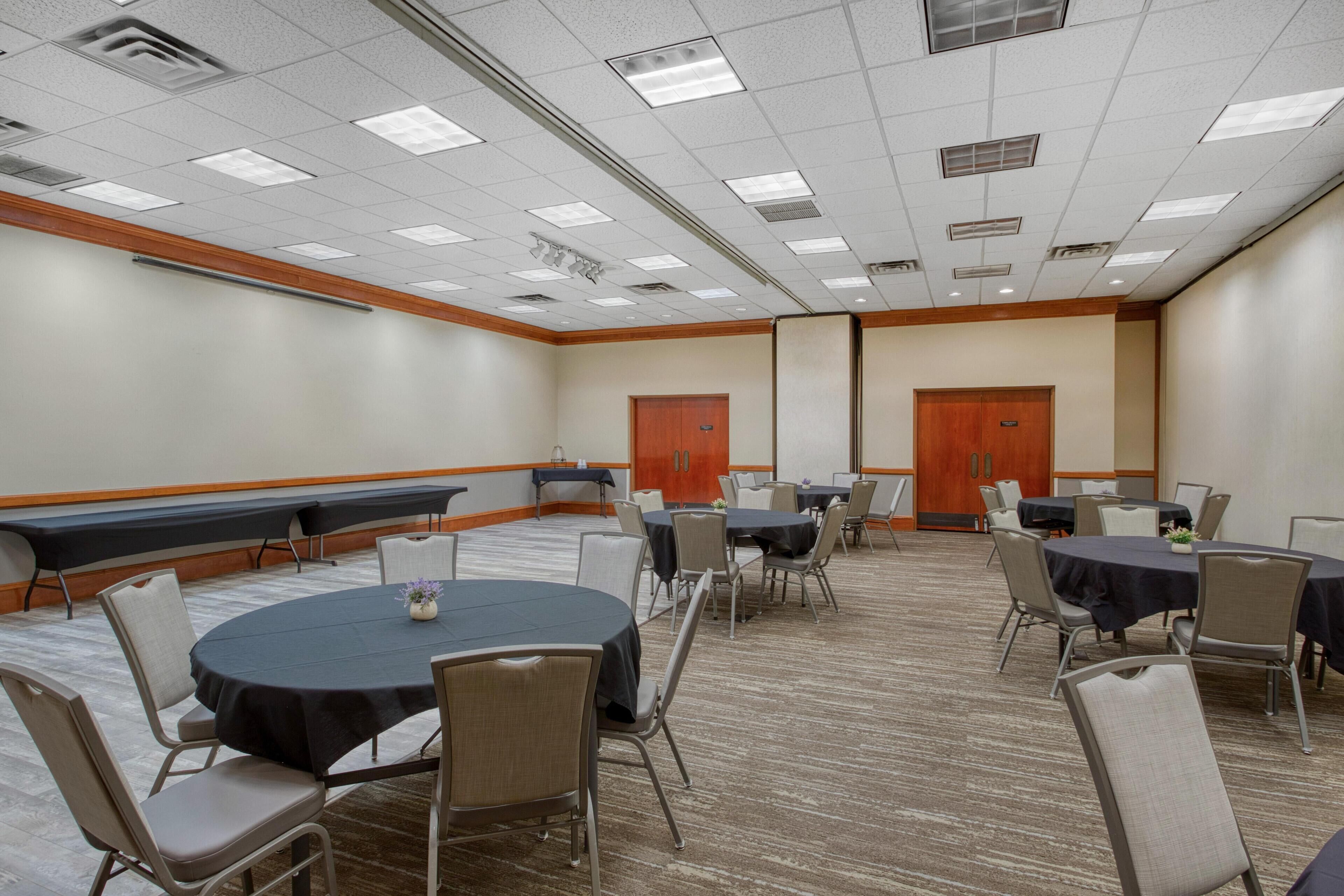 A conference room with round tables and chairs, a carpeted floor, and a high ceiling with fluorescent lighting.