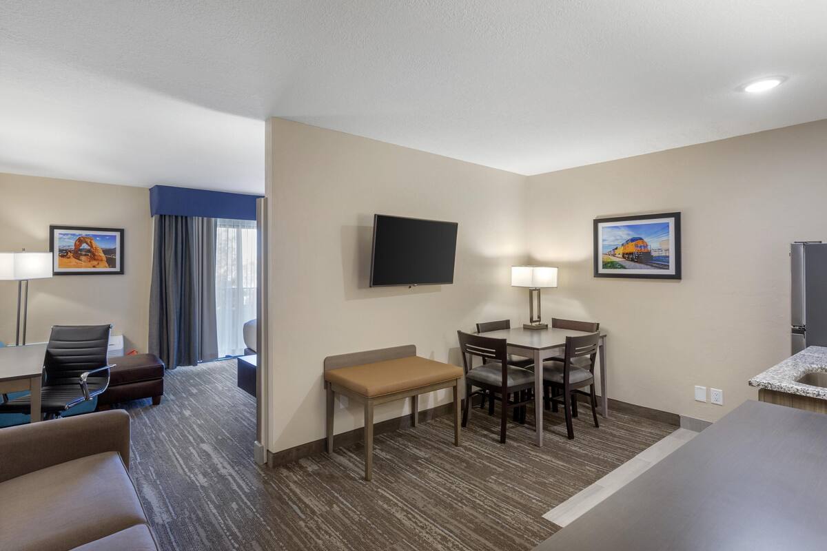 A hotel room with a bed, a desk, a chair, a small table, a lamp, and a TV on the wall.