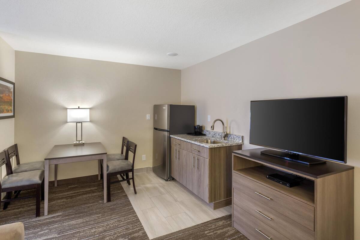 A compact kitchen with a refrigerator, microwave, and a flat-screen TV on a wooden stand.