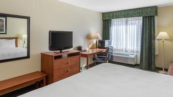 A hotel room with a bed, a desk with a computer, a television, and a window with curtains.