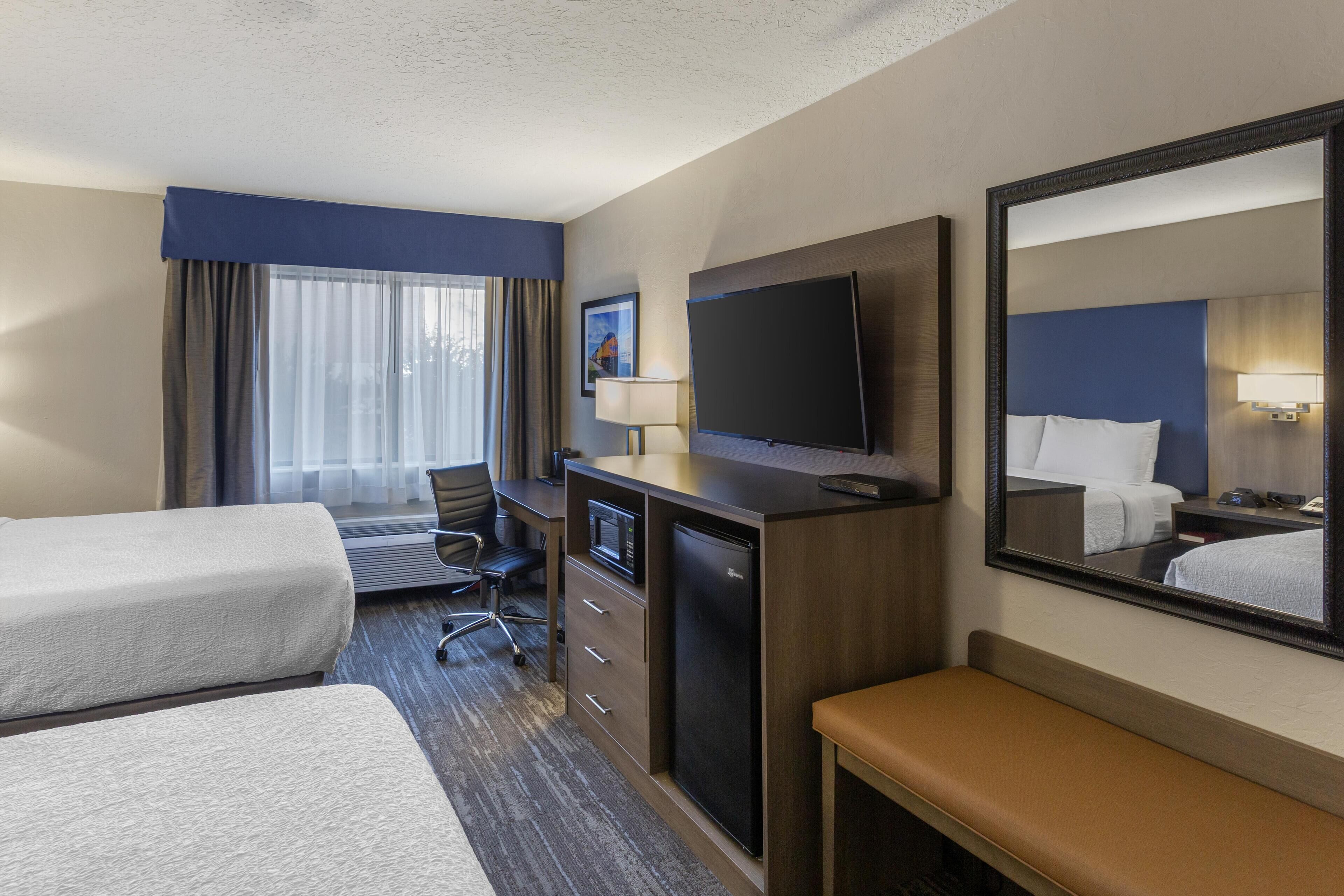 A hotel room with two beds, a desk with a computer, a television, and a large mirror.