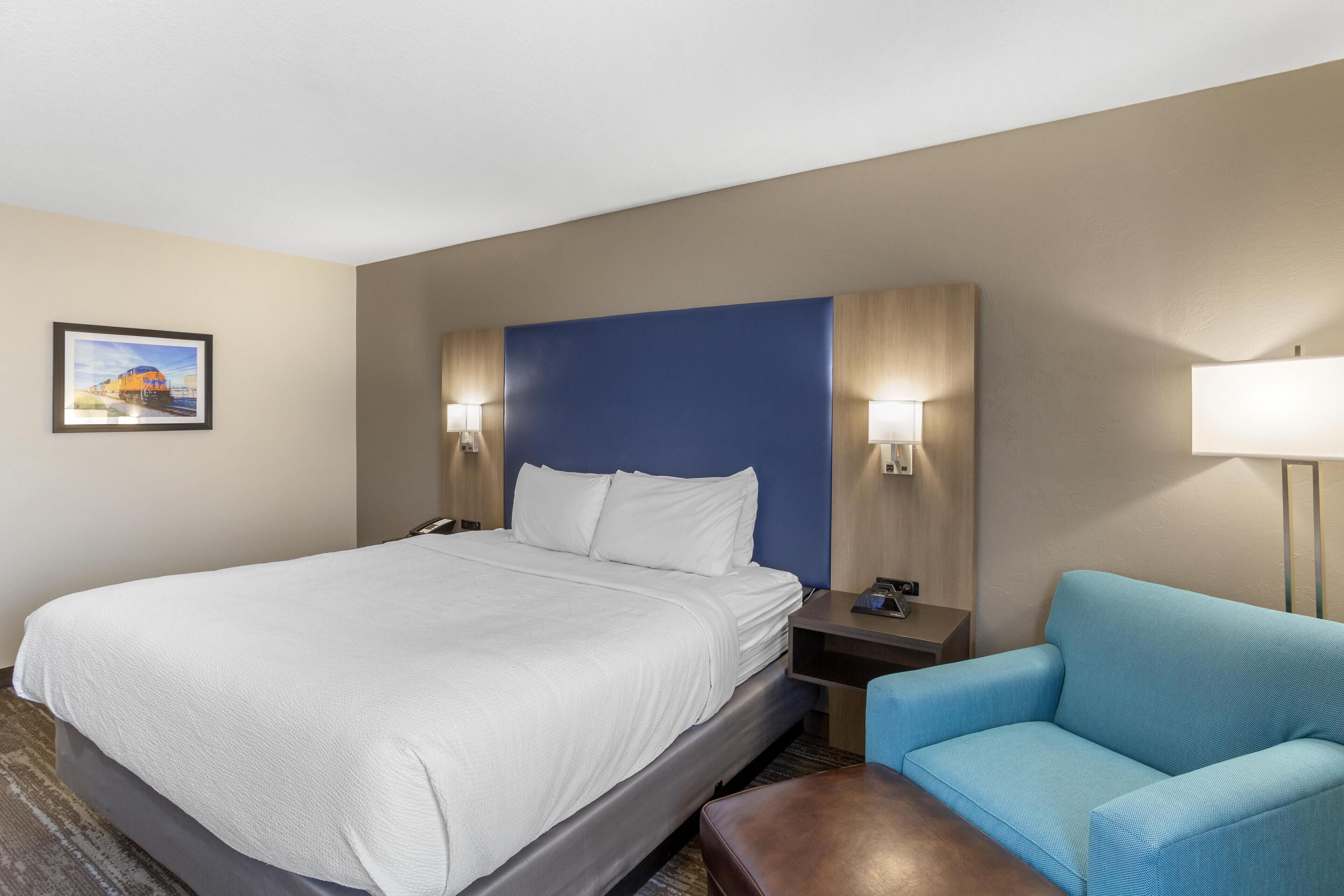 A hotel room with a large bed, two bedside lamps, a blue accent wall, and a blue armchair.
