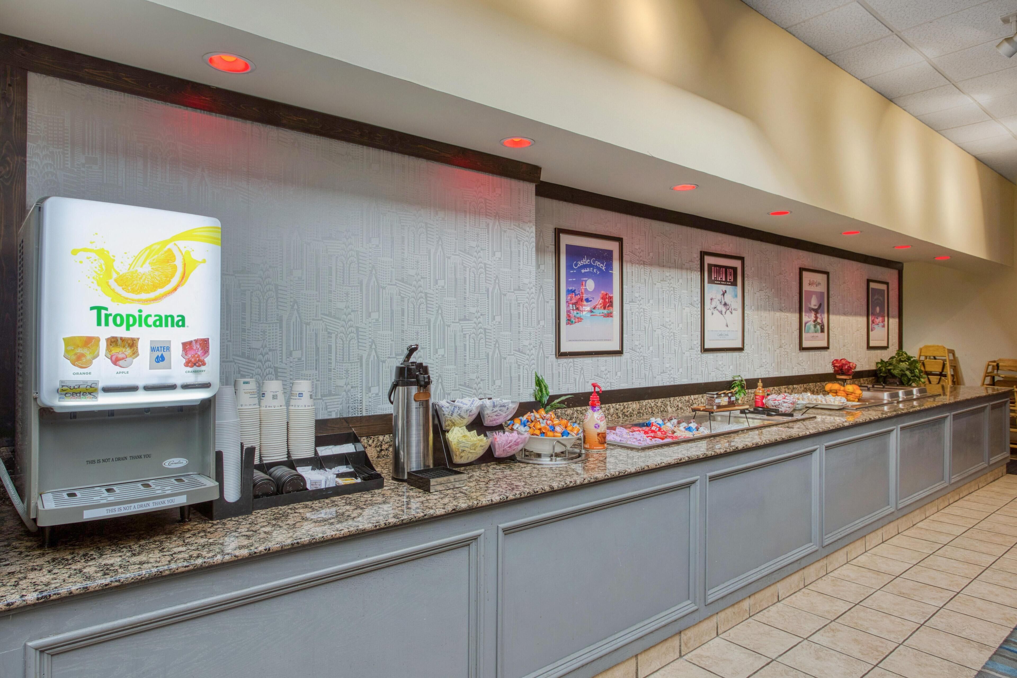 A Tropicana juice dispenser, a coffee machine, and a variety of food items on a buffet counter in a hotel lobby.