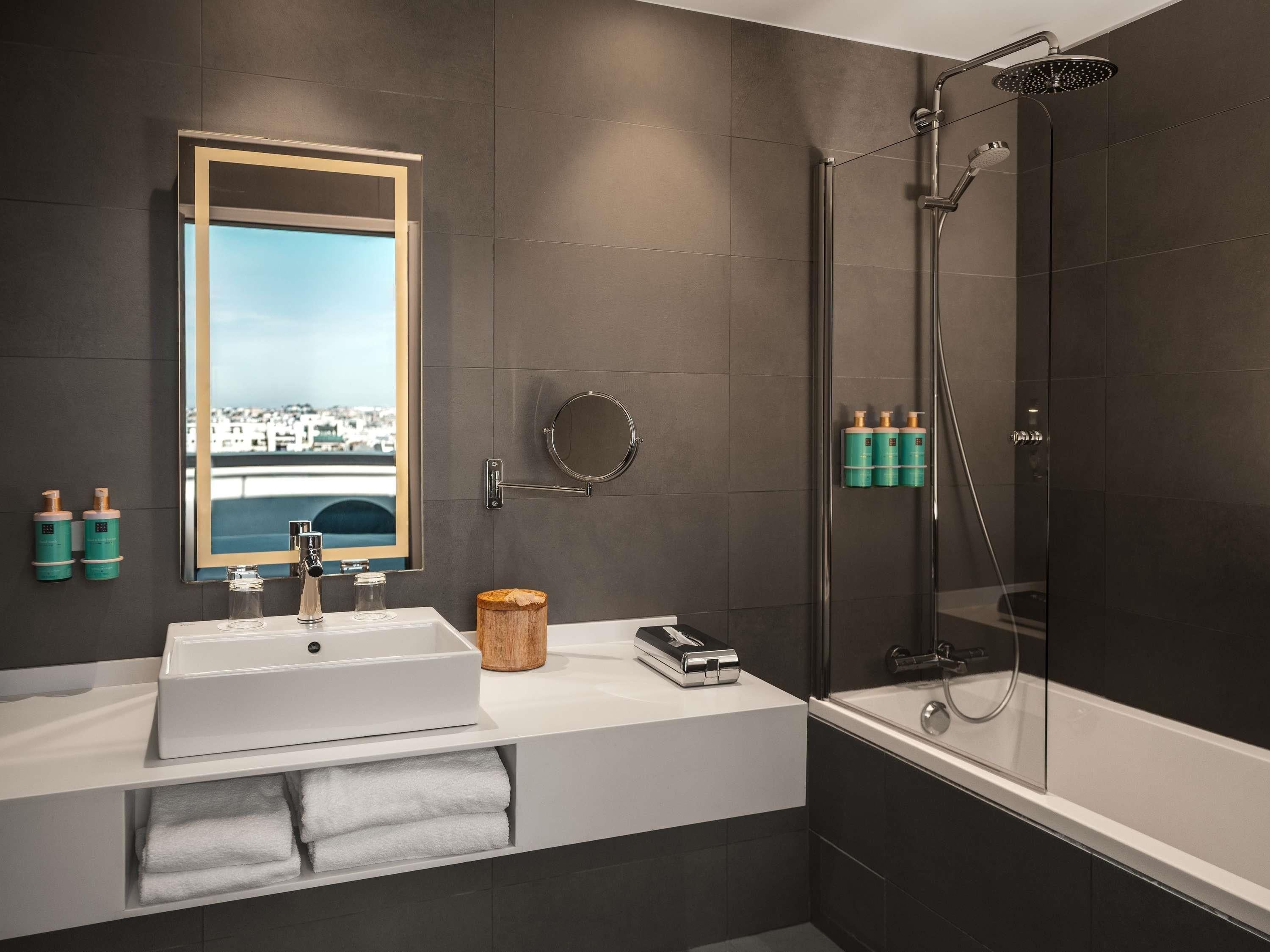 A modern bathroom with a large mirror, a shower, and a sink.
