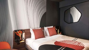 A modern hotel room with a large bed, a round table, a mirror, and a wall with a unique pattern.