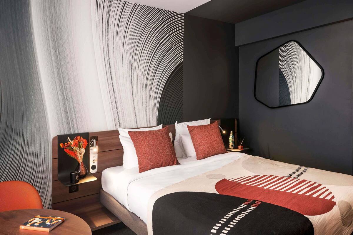 A modern hotel room with a large bed, a round table, a mirror, and a wall with a unique pattern.