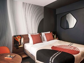 Ein modernes Hotelzimmer mit einem großen Bett, einem runden Tisch, einem Spiegel und einer Wand mit einem einzigartigen Muster.