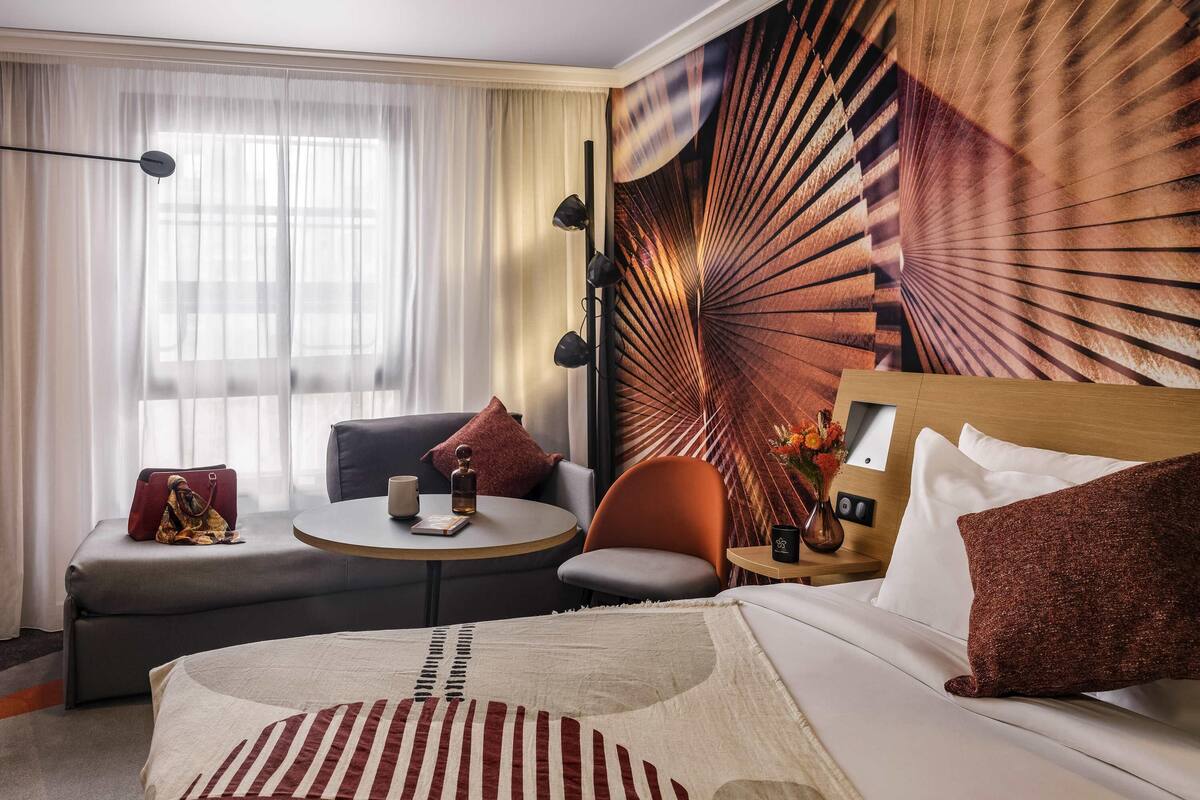 A hotel room with a bed, a sofa, a round table, and a wall with a radial pattern.
