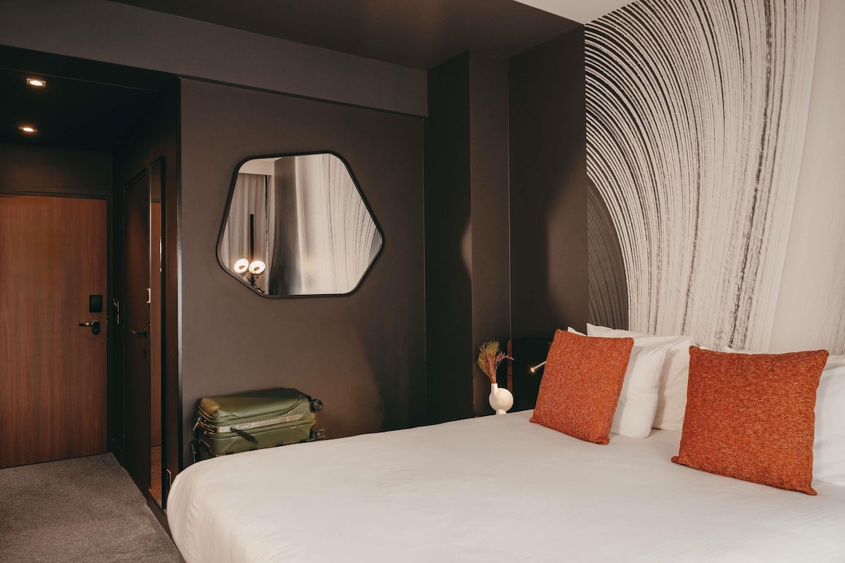 A hotel room with a bed, a mirror, a suitcase, and a wall with a textured design.