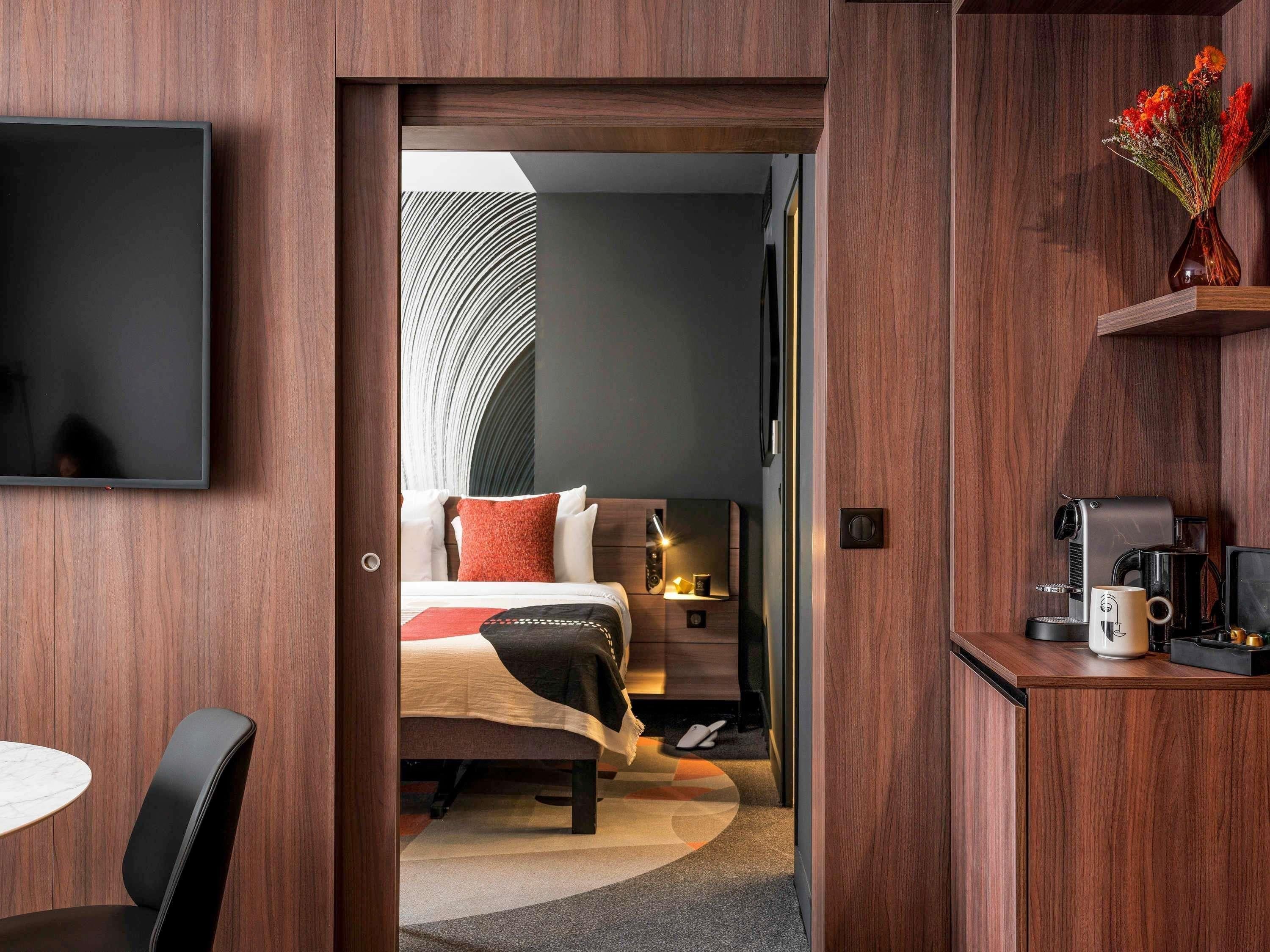 Quarto de hotel com cama, mesa de cabeceira, luminária e cantinho para café.