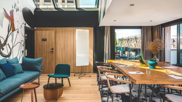 Un interior moderno con una mesa de comedor de madera, sillas color turquesa, un sofá color turquesa y un separador de vidrio.